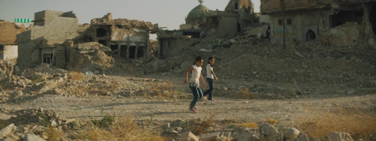 Two children play by the broken down buildings