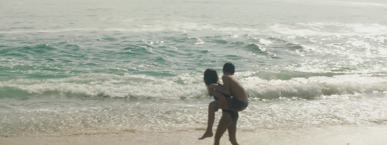 Girl piggybacks boy and plays in the surf
