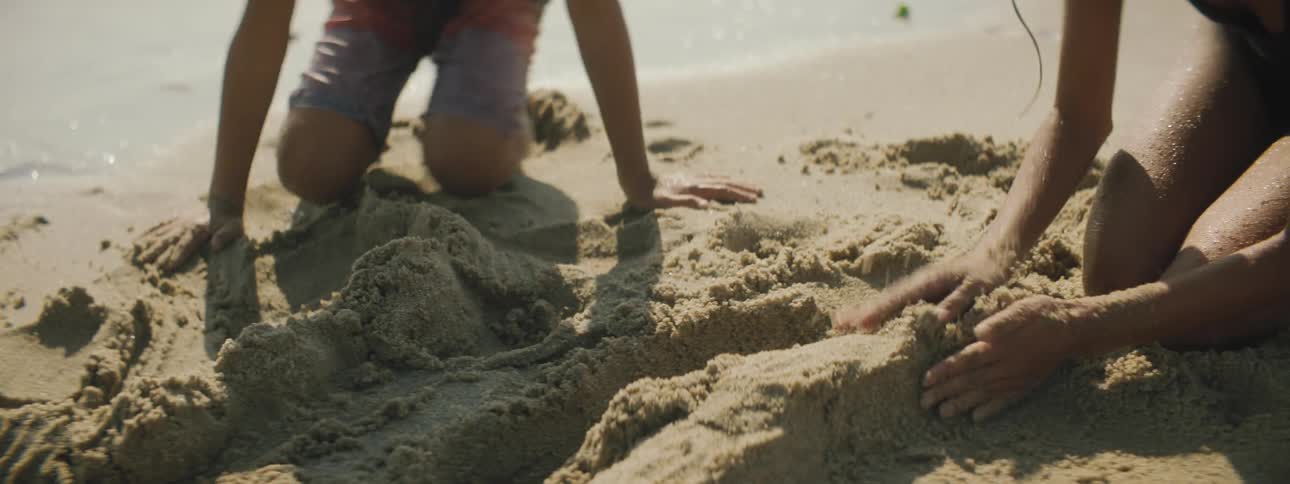 A boy and girl play in the sand on a beach and construct an object with the sand