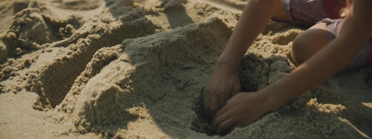 A boy and girl in swimsuits digging and playing in sand on a beach