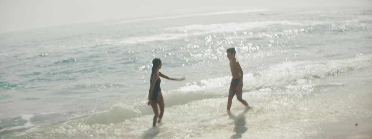 Girl and boy in swimming attire play in an out of surf on misty day