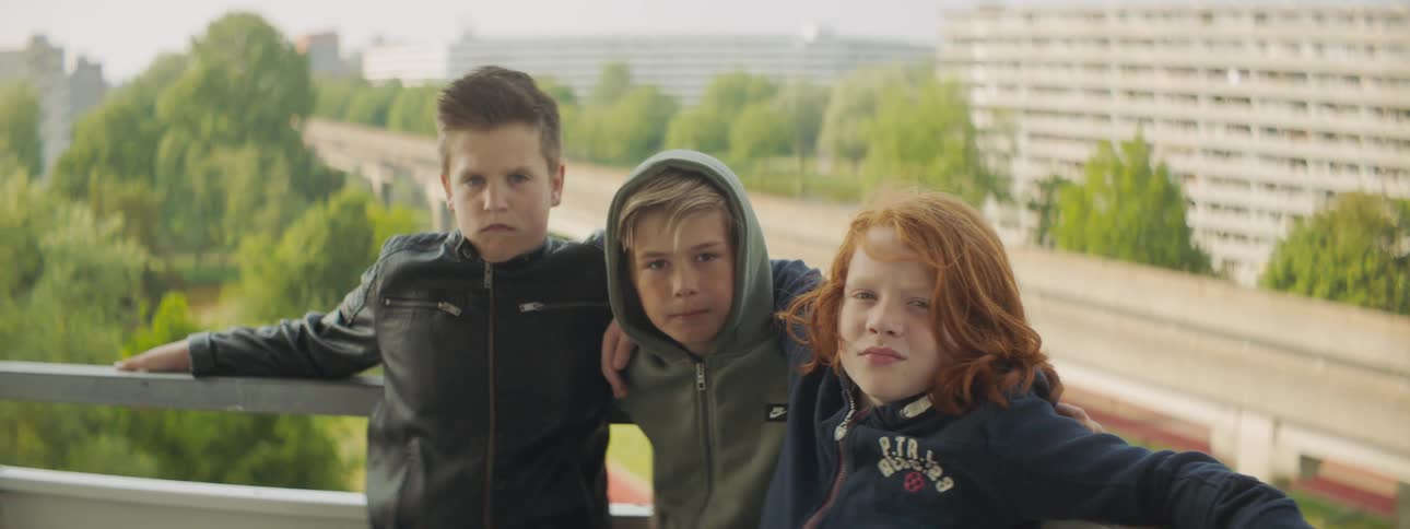 Three boys pose with arms around each other against rail near overpassbordered by mist covered buildings