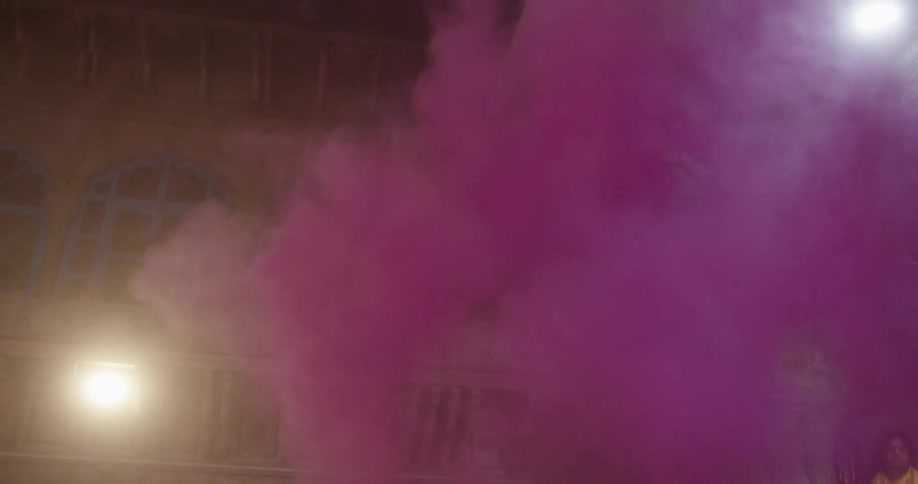 A man throws purple dust over a crowd