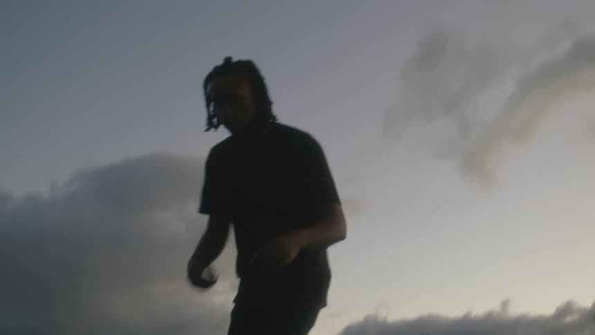 A man dances on a hillside under a cloudy evening sky