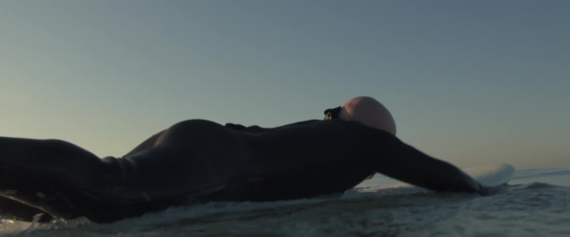 A man paddles through the ocean while lying down on his surfboard