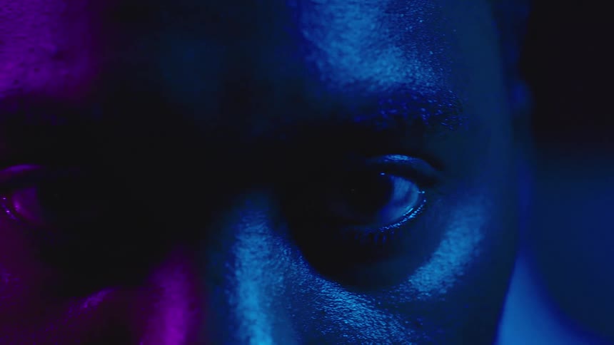 A dark blue light shines on a mans face