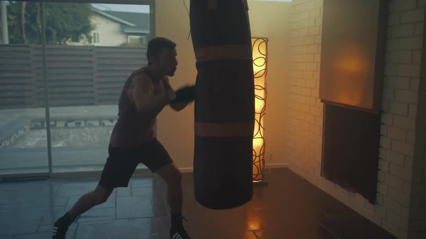 A man punches a boxing bag hanging in a gym at his house
