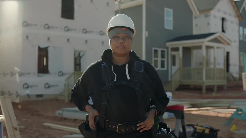 A female construction worker stands and poses in front of several homes that are under construction
