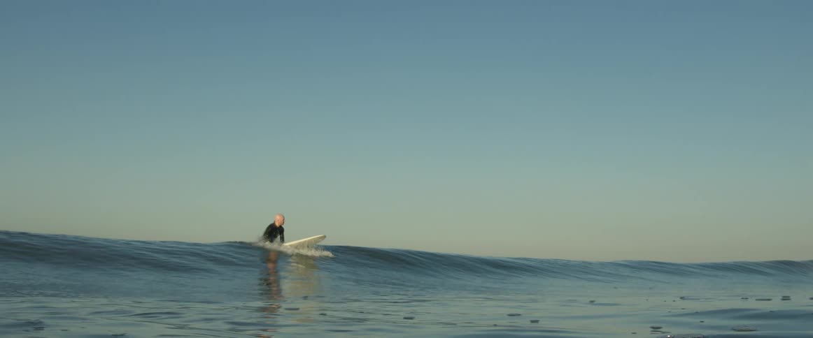 A person is surfing on the ocean water at dusk