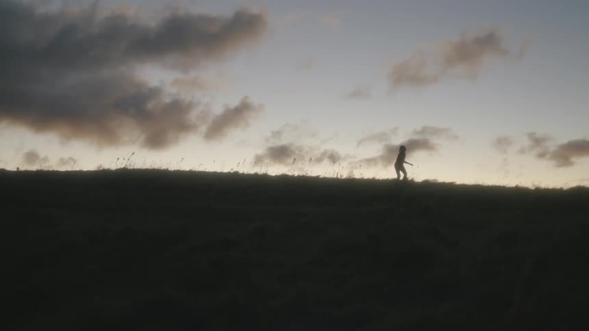A person stumbles while walking across a hill in the evening