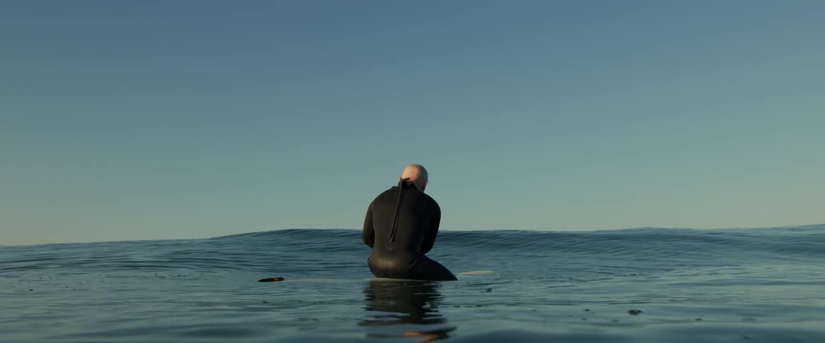 A man in a wet suit floating on a surfboard at dawn