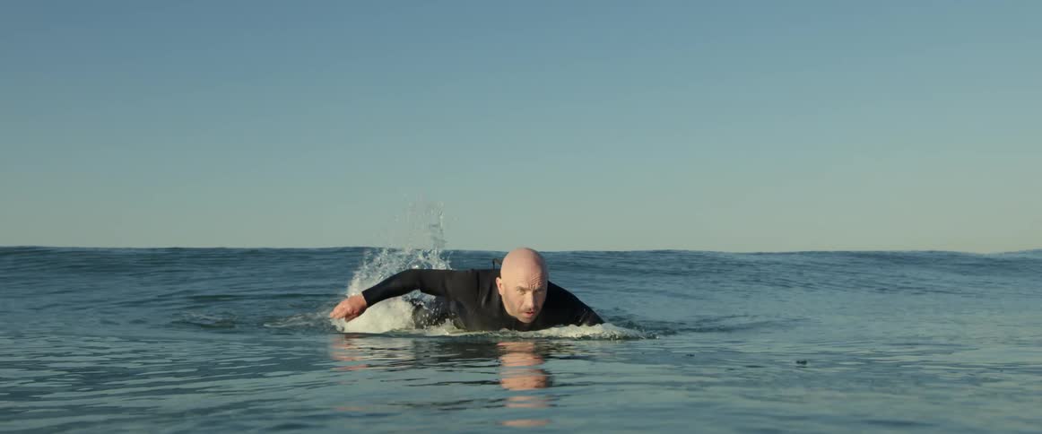 An older white man is surfing on the ocean in the middle of the day