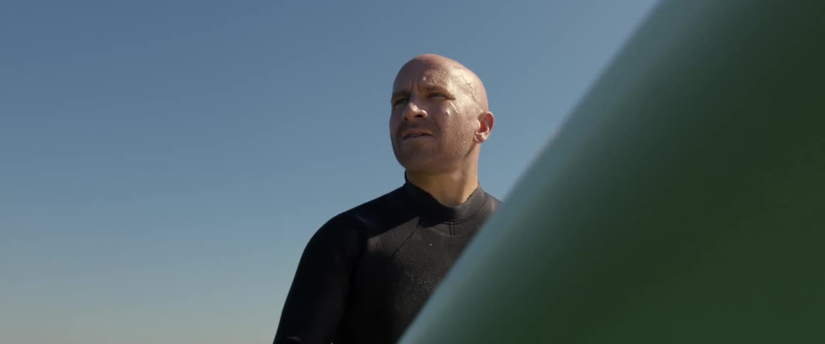 A man in a wetsuit holds a surfboard while standing outdoors during the day