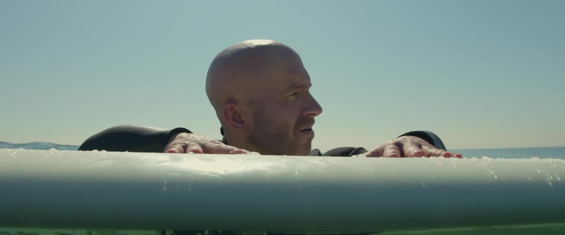An older white man is in the ocean holding on to his surf board
