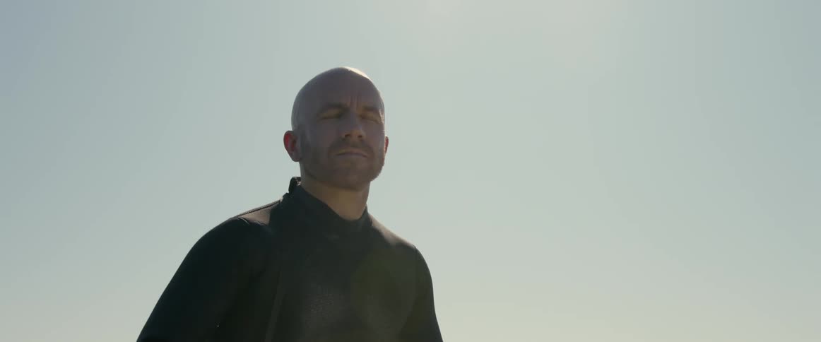 A man sitting on a surfboard bobs up and down with the motion of the ocean with eyes closed