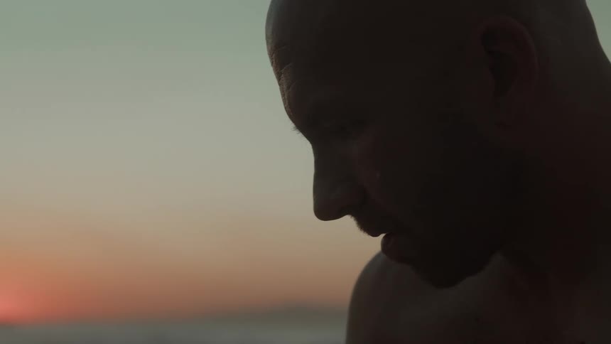A man wipes off his surfboard on the beach at sunset