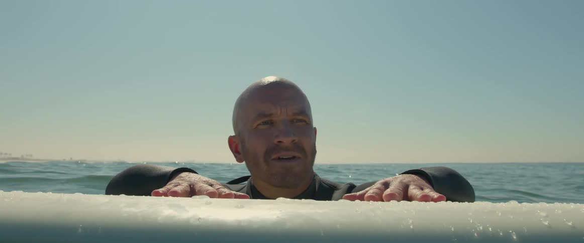 A man is in the ocean hanging onto his surfboard as he looks around