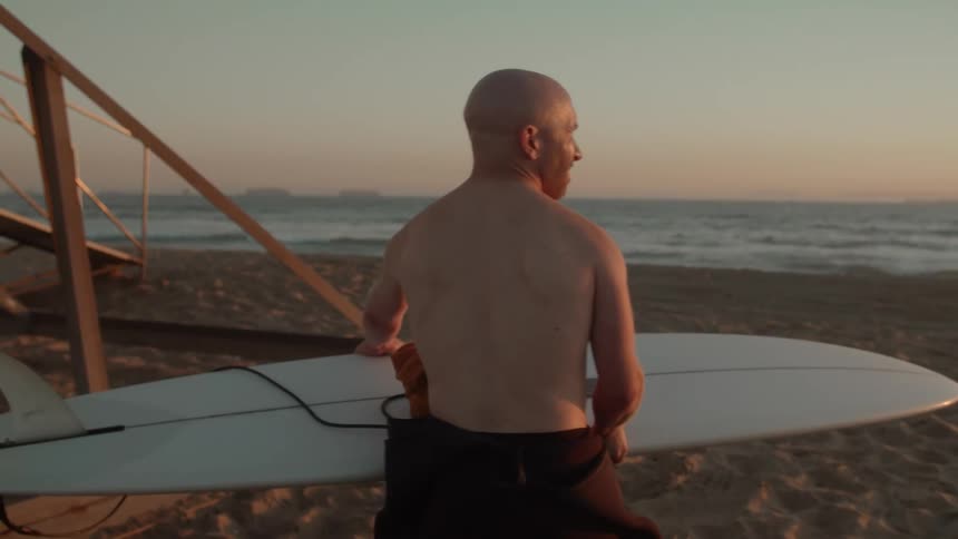 A man puts down his surfboard on the beach