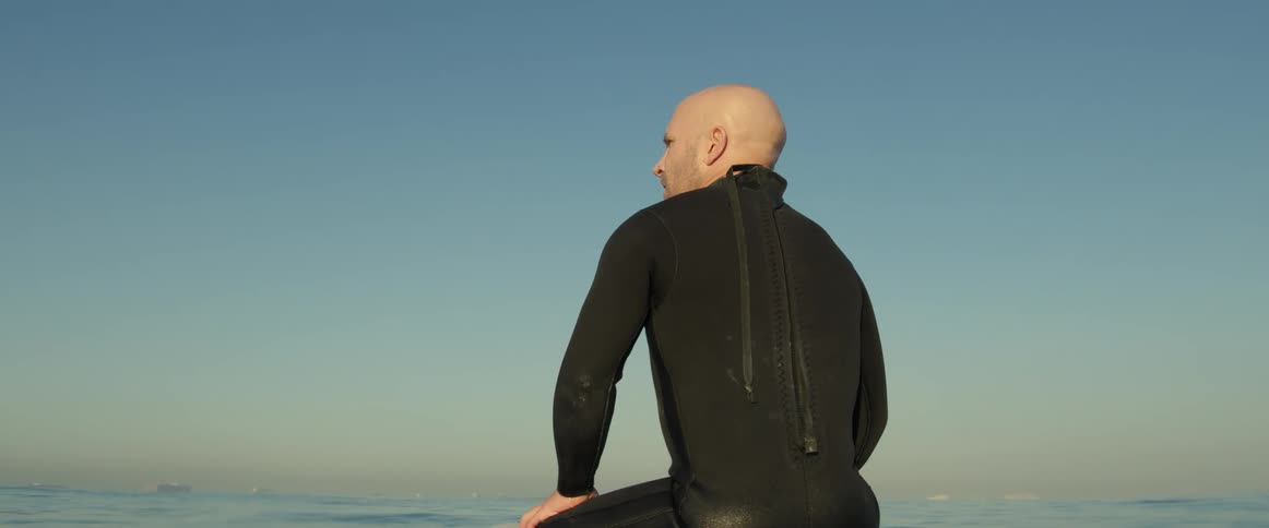 A man sits on his surfboard in the ocean