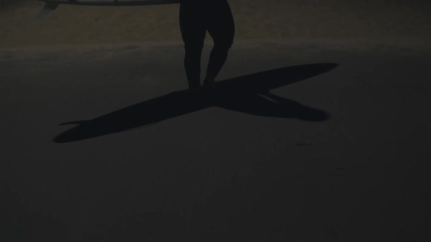 A surfer carries his board at night on the beach
