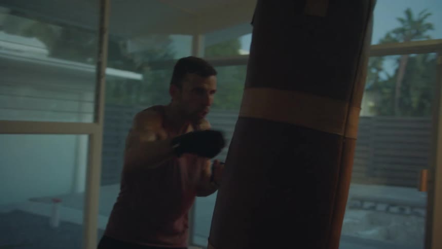A man is inside a room with large windows working out with a punching bag