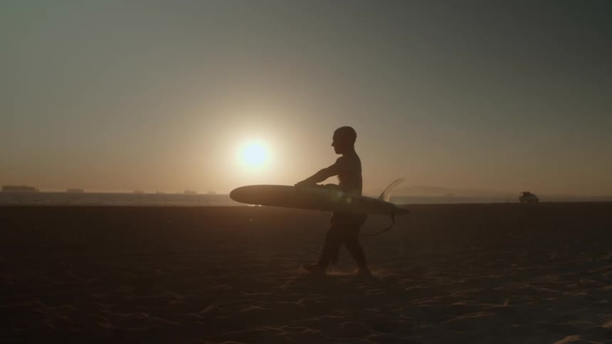 A man is walking with his surf board during sunset