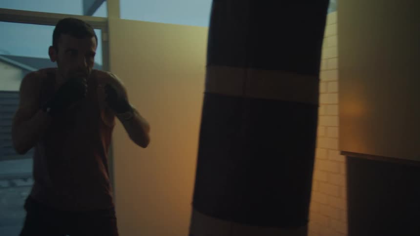 A man is inside a room with large windows working out with a punching bag