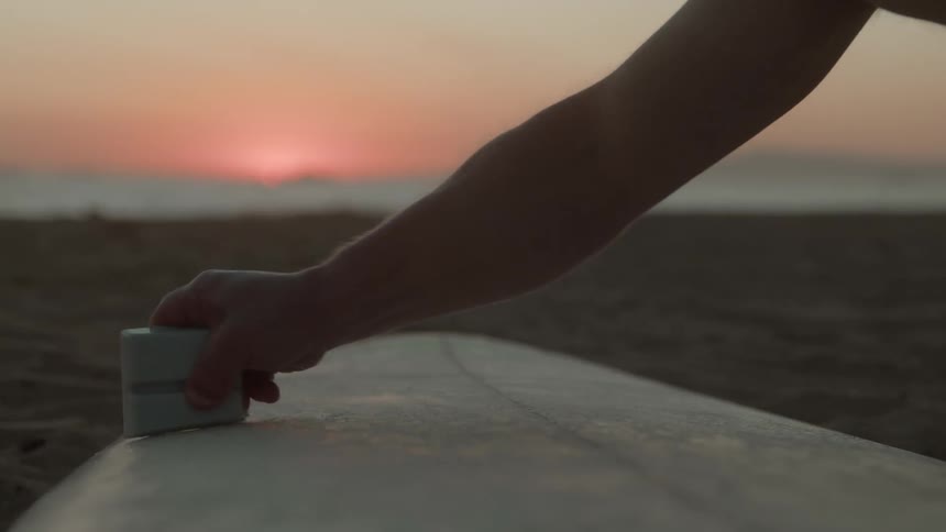 A person is cleaning their surfboard while the sun is setting