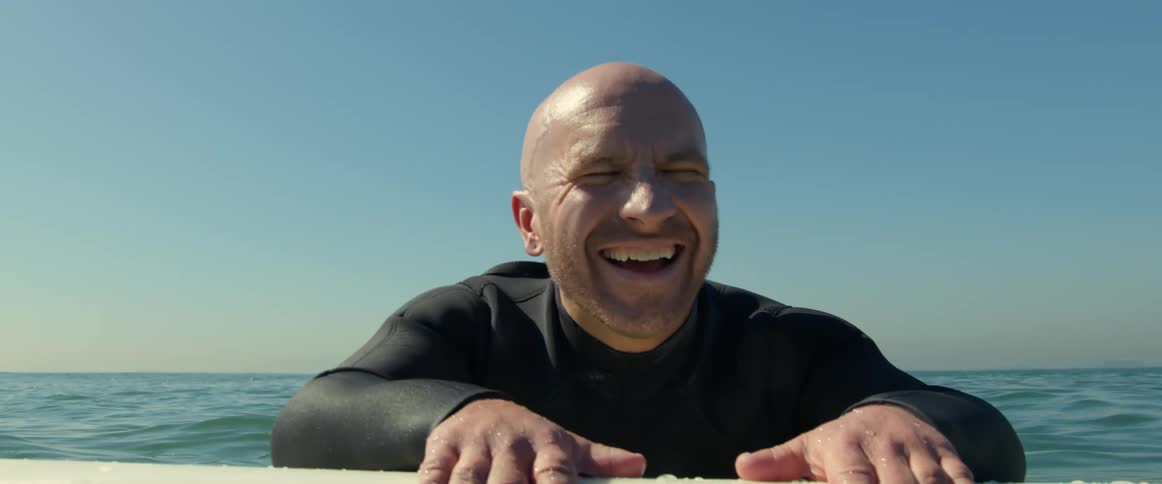 A man smiles while lying on his surfboard in the water