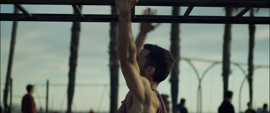 A man climbs across a set of monkey bars on a beach during the day