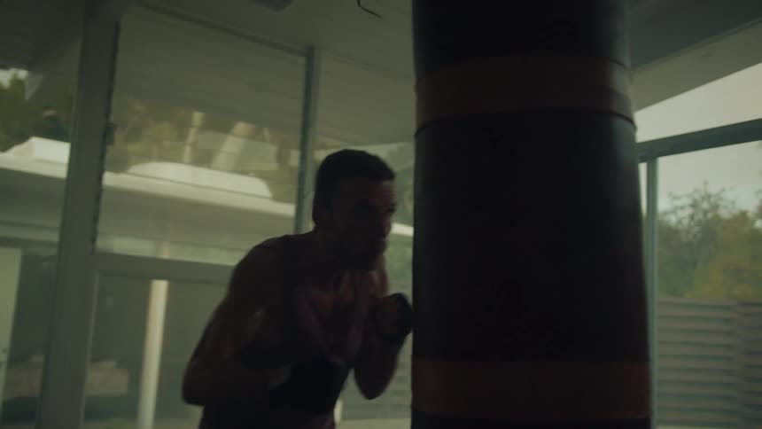 A man wearing boxing gloves is punching a hanging bag