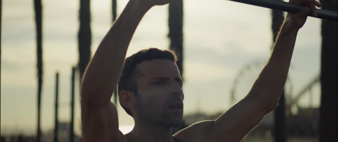 A man working out at the beach reaches up for the pull up bar