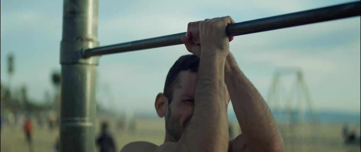 Man exercises on beach as other people move along shore