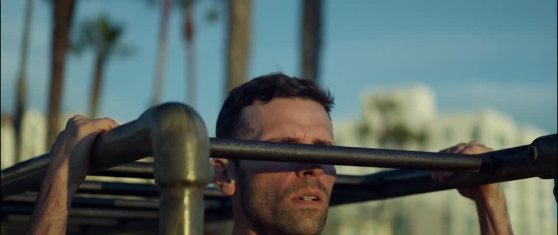A man does pull ups on bars at a park