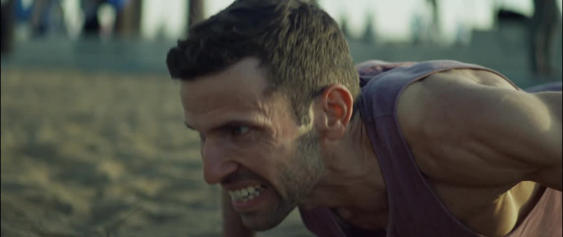 A man is doing pushups in the sand at the beach