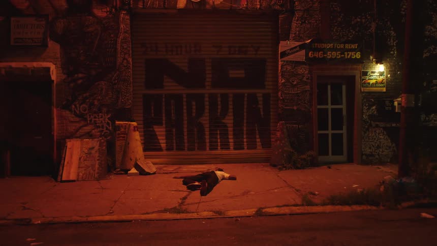 Man lies on ground on sidewalk near graffiti covered building at night