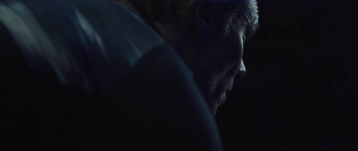 Man pedaling on a static bicycle inside a dimly lit room against a dark background