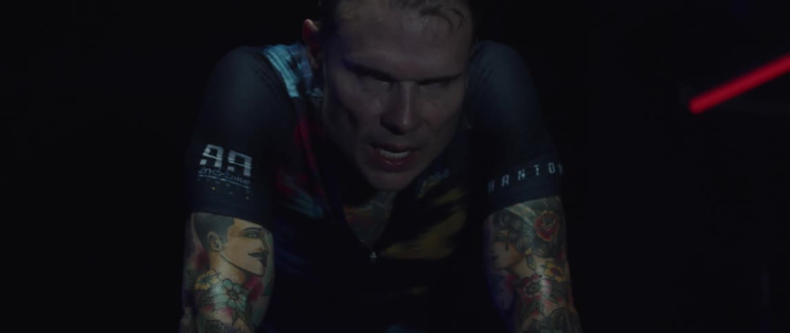 Focused sweaty man wearing a cycling jersey exercising on a stationary bike in a dark room