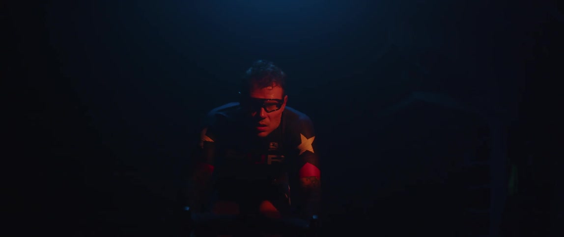 A man wearing a starry shirt pedals a bike under a light