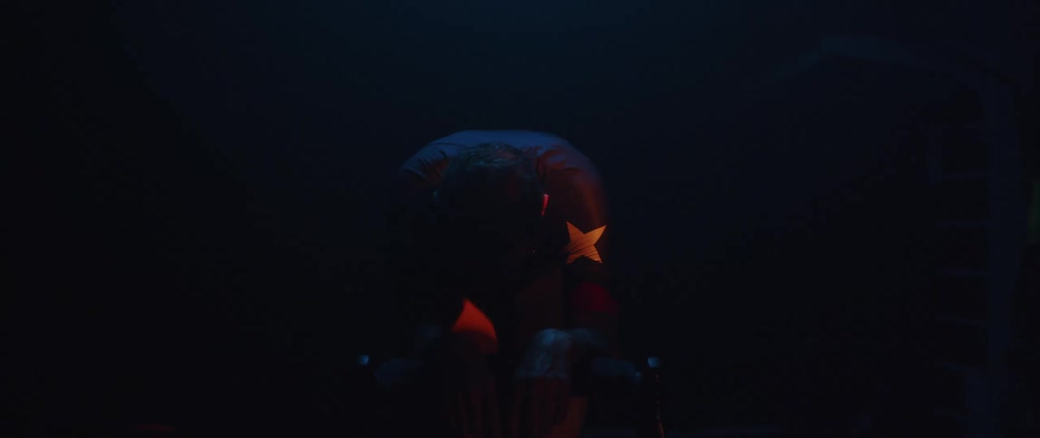 A sweaty man riding a stationary bike in a dark room