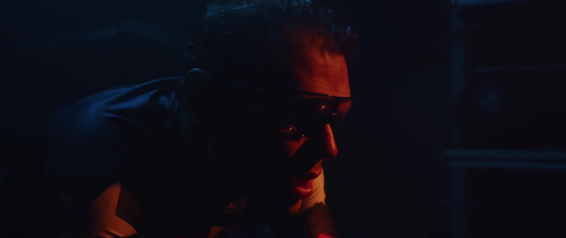 Man wearing sunglasses pedaling a static bicycle inside a dimly lit room