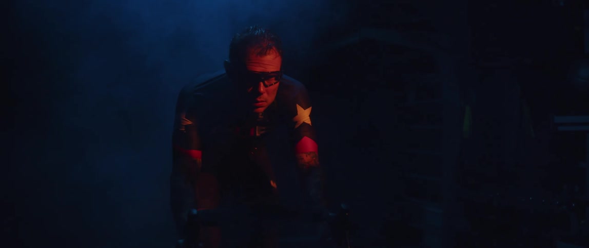 A man cycles on an exercise bike in a dark room