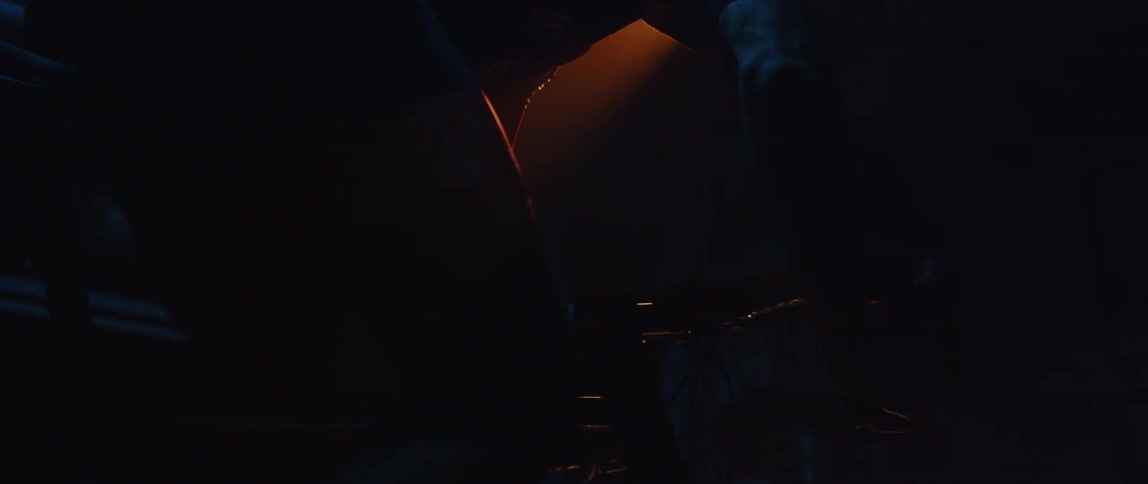 Silhouette of a man pedaling a static bicycle inside a dimly lit room under a spotlight