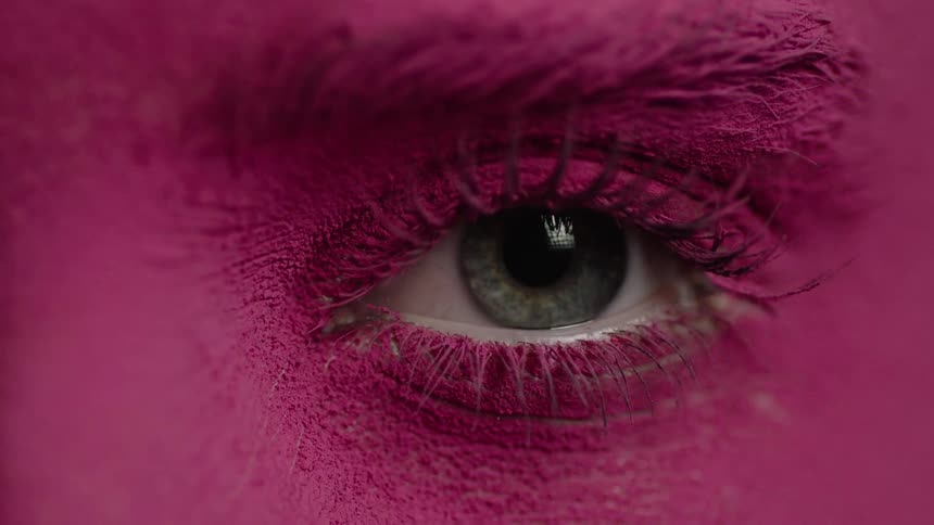 A woman with her face covered in a thick pink powder opens her eyes