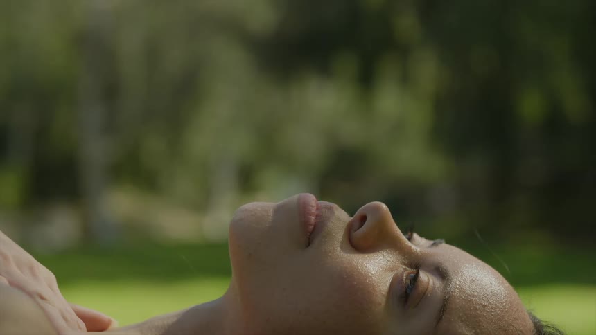 The face of a woman lying in the grass sunbathing hand touching her neck