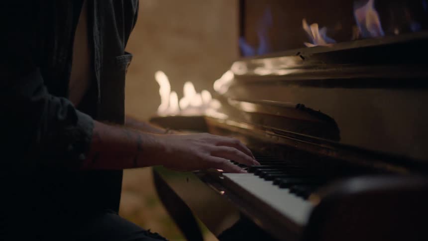Man plays piano lit with flames