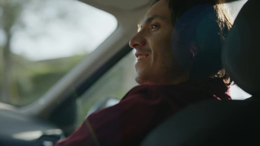 A man sitting in the passenger seat in the car looks over and smiles at the driver