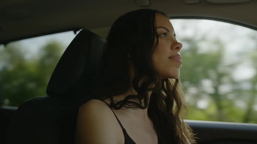 A woman with curly hair smiles subtly as she drives in a car
