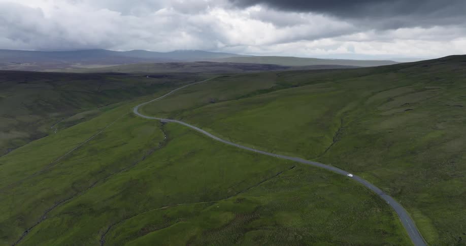 Car drives along highway toward misty mountains under dark clouds