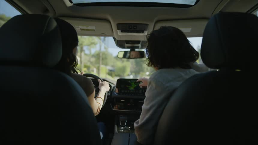 Man and woman drive through sunny neighborhood in an SUV